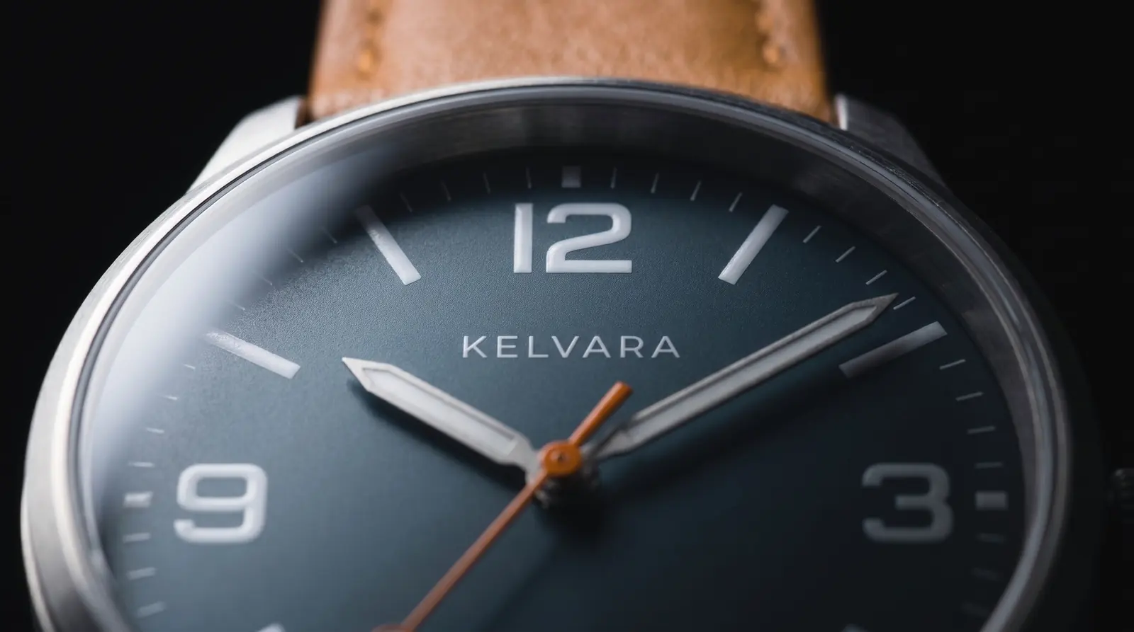 Close view of the slate dial: numerals 12, 3 and 9 in view, slim batons, KELVARA below the 12, white sword hands and the orange seconds hand.