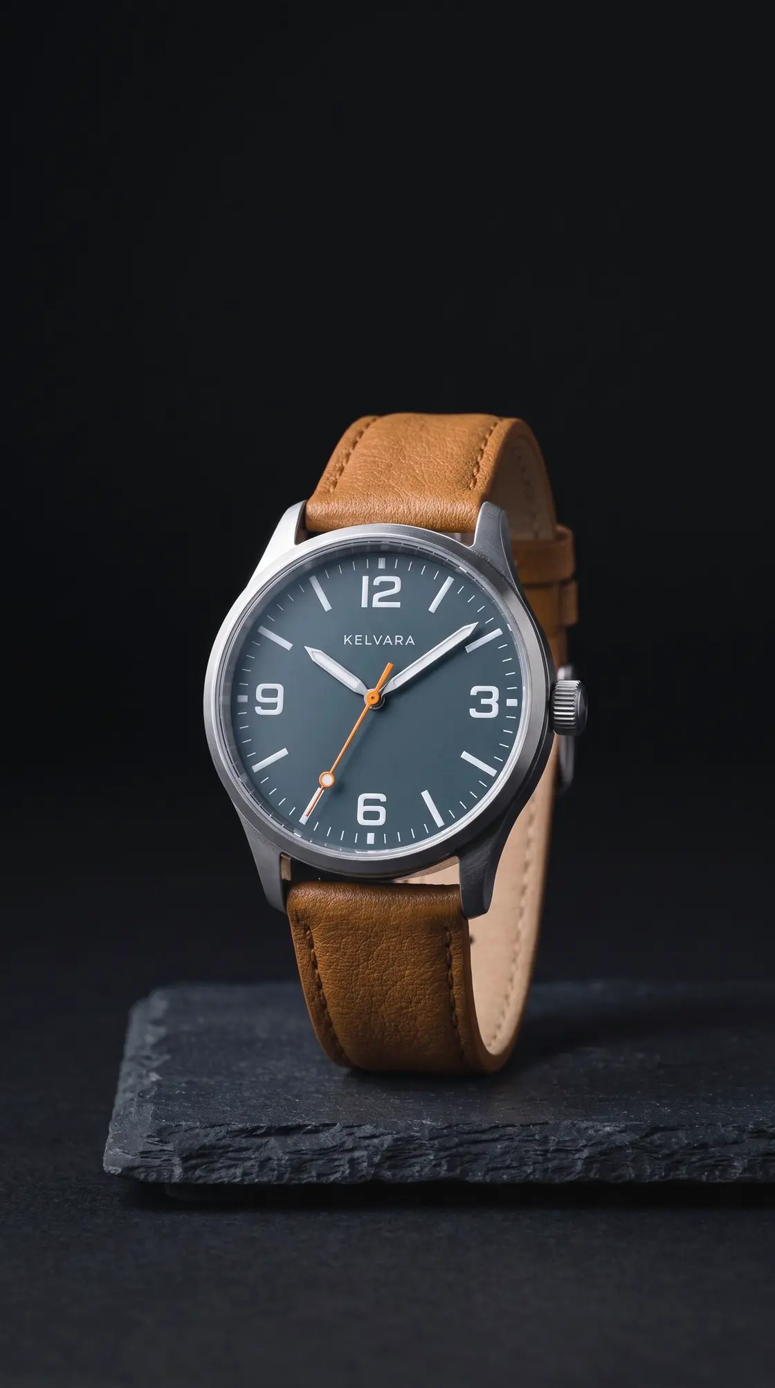 The Kelvara upright on a slate block, front view: numerals at 12, 3, 6 and 9, the orange seconds hand and the tan strap.